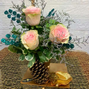 Centro de mesa navideño con rosas suaves, piñas doradas y acentos azules