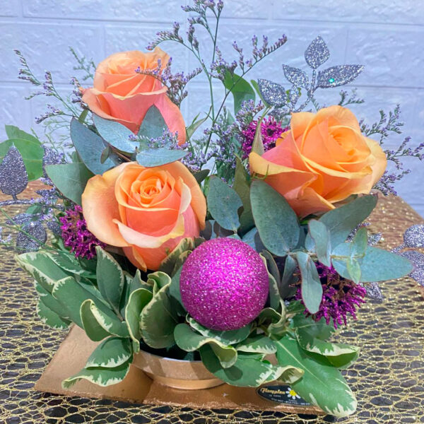 Centro de mesa navideño con rosas durazno, follaje y esfera magenta brillante